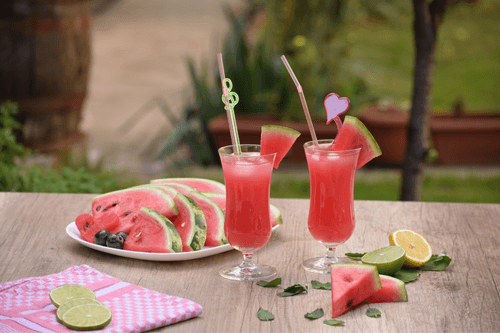 Gesneden watermeloen op een tafel in de tuin. Op de tafel staan twee glaasjes met watermeloensap. Watermeloen Exotisch Fruit