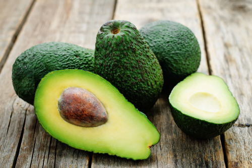 Avocado's gelegen op hout. Een avocado is doormidden gesneden zodat je het groene vruchtvlees kan zien.