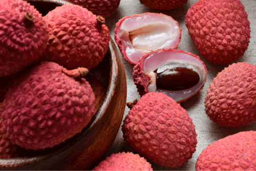 Lychee fruit gelegen in een houten schaaltje. Een lychee is opgesneden zodat je het witte vruchtvlees en de pit kan zien